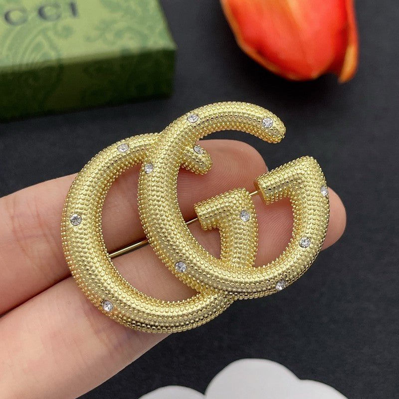 Gold Gucci earrings held in a hand with a dark background