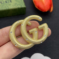 Gold Gucci earrings held in a hand with a dark background