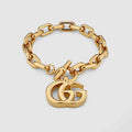 Gold chain bracelet with a heart-shaped Gucci logo charm on a light gray background